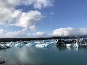 A 10-day Itinerary to Iceland's Ring Road 5 Glacial blue water in the foreground gives way to the icebergs of the Jokulsarlon lagoon. There are dizens of icebergs in hues of gray, black, light blue and white.
