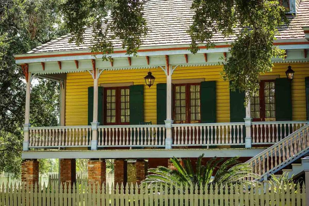 Driving from Texas to Florida? Best Boutique Hotels in New Orleans Off of I-10 3 A picture of the Laura Plantation. The house is yellow with white trim and red accents. The shutters are green and there is a gray tiled roof. A picket fence surrounds it.